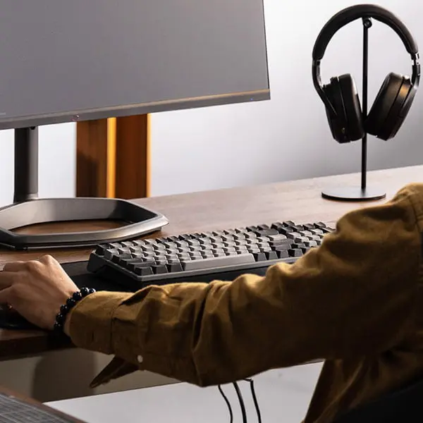 Utilisateur devant un écran et un clavier, avec plusieurs périphériques connectés sur un bureau Cette image montre un poste de travail informatique avec écran, clavier, casque audio et câbles USB visibles, représentant une configuration utilisateur typique. Elle accompagne la recommandation de débrancher tous les périphériques USB lors d’un dépannage de démarrage PC. Des clés USB, disques externes ou périphériques audio/vidéo peuvent interférer avec le boot système, surtout si le BIOS tente de démarrer sur un support externe. Cette photo renforce visuellement l’importance de simplifier la configuration lors de la recherche de la cause d’un démarrage bloqué.