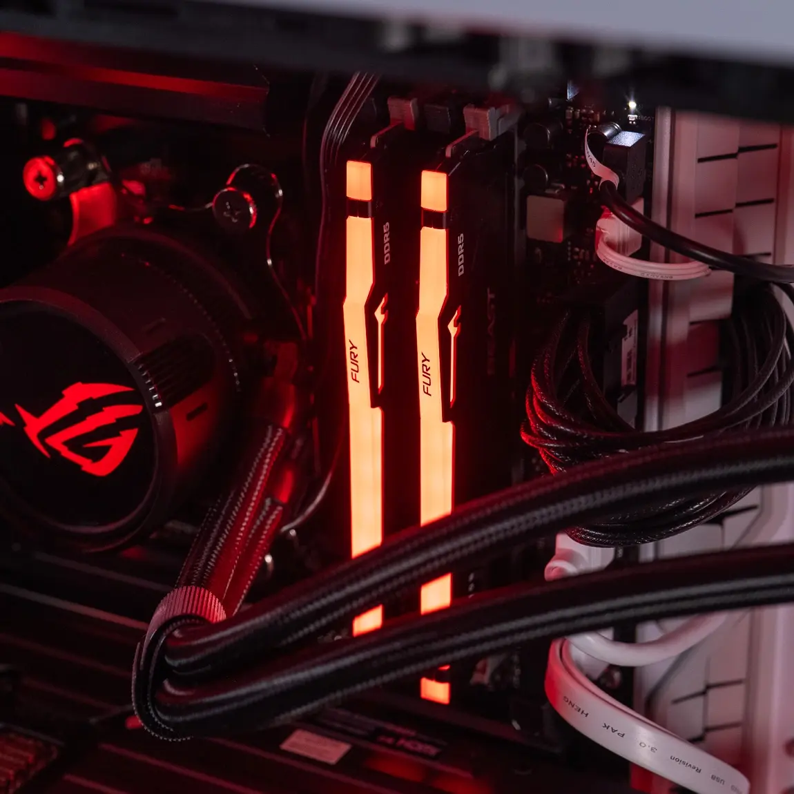 Deux barrettes de RAM DDR5 Kingston FURY installées sur une carte mère dans un PC gaming éclairé en rouge Cette image montre l’intérieur d’un PC gamer, avec deux barrettes de RAM DDR5 Kingston FURY installées sur une carte mère ASUS ROG, entourées de câbles gainés et d’un refroidissement liquide RGB. Elle illustre l’étape de diagnostic mémoire recommandée lorsqu’un ordinateur ne démarre pas. Une barrette mal installée ou défectueuse peut suffire à empêcher le démarrage du système. Il est conseillé de tester chaque module individuellement, en changeant de slot DIMM si nécessaire, afin d’identifier un éventuel défaut matériel. Cette vérification est simple à effectuer et permet d’isoler rapidement l’origine du problème.