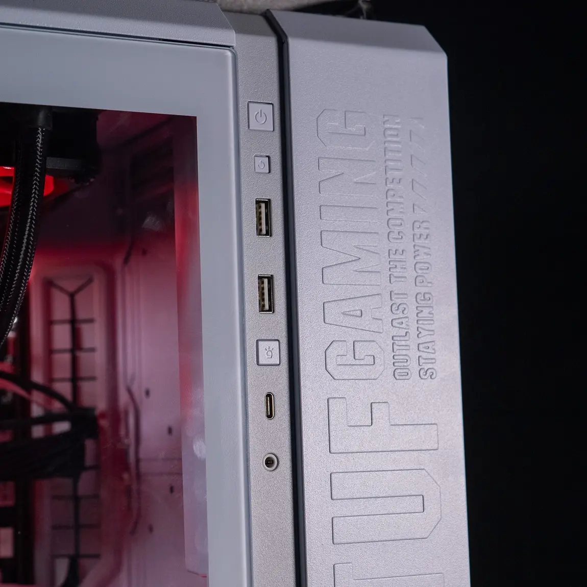 Bouton d’alimentation et ports USB en façade d’un boîtier PC TUF Gaming argenté Cette photo montre la façade d’un boîtier TUF Gaming, avec le bouton d’alimentation, les ports USB et un connecteur audio accessibles. Elle illustre l’étape de vérification du bouton Power lors d’un diagnostic de panne de démarrage PC. Si aucune LED, ventilation ou signal sonore ne se déclenche, il est important de tester le bouton Power lui-même, ou d’utiliser le bouton Reset si présent. En cas de doute, un démarrage manuel via les broches Power SW de la carte mère peut être envisagé (méthode réservée aux utilisateurs expérimentés). Cette image renforce la vérification matérielle en surface avant d’envisager des interventions internes.