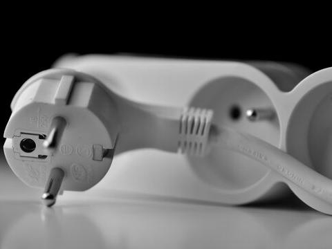 Gros plan sur une prise électrique européenne blanche avec une multiprise en arrière-plan Cette image présente une prise électrique standard avec une multiprise en arrière-plan, illustrant la vérification de l’alimentation secteur dans le cadre d’un diagnostic de démarrage PC. Il est recommandé de brancher l’ordinateur directement sur une prise murale, sans utiliser de multiprise ou rallonge, afin d’éviter les perturbations électriques ou pertes de tension. Cette photo complète visuellement la procédure consistant à tester une autre prise à l’aide d’un appareil fonctionnel comme une lampe, pour exclure toute panne d’origine électrique.