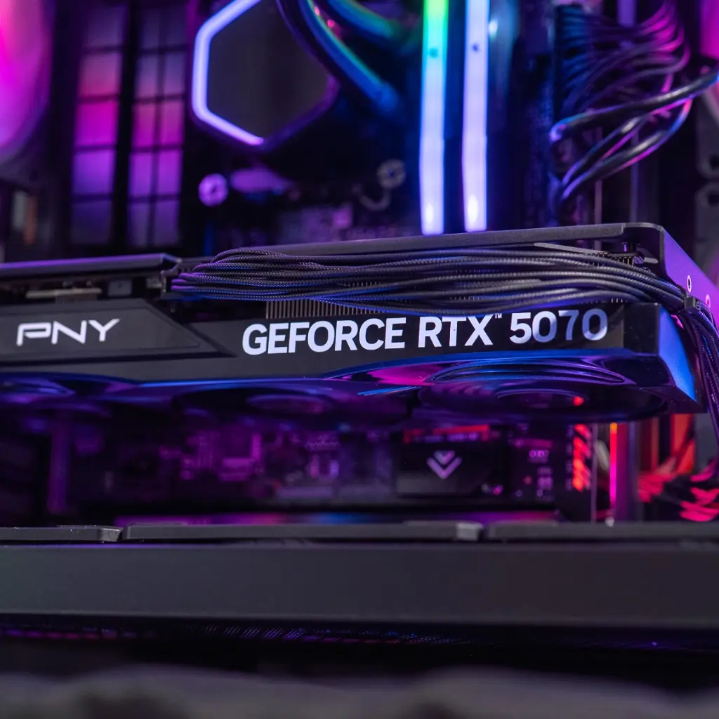 Gros plan sur la carte graphique PNY GeForce RTX 5070 installée dans le PC gamer Aqua, révélant ses caloducs en cuivre et son éclairage ambiant rose et bleu